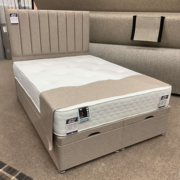 Beige fabric Ottoman bed with matching headboard and mattress, shown with the base closed in a showroom setting.